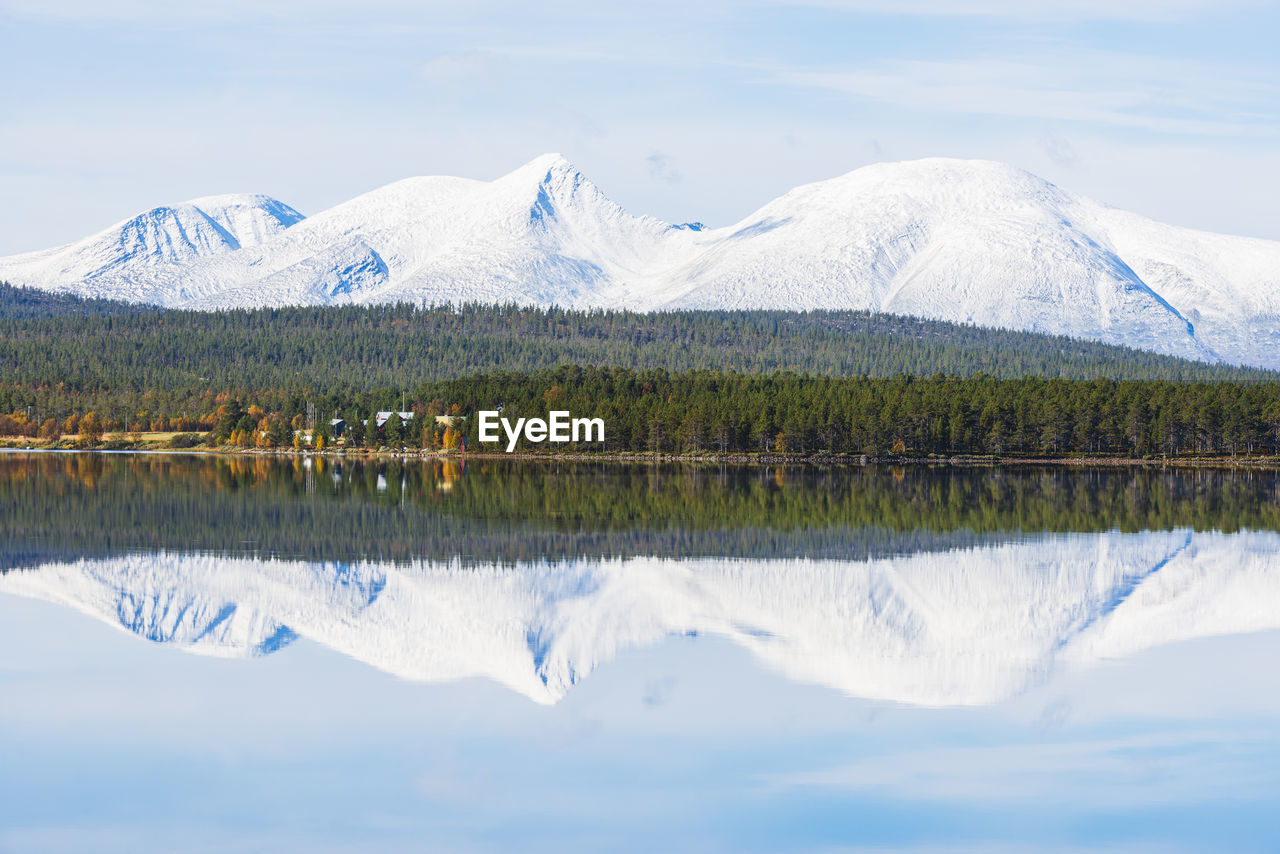 Snowy mountain and a green forest reflected in a still lake