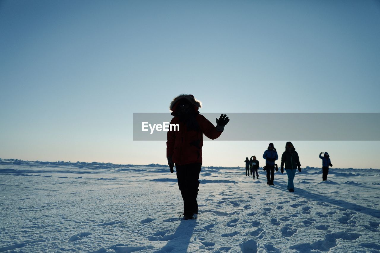 Silhouette hikers walking on snow covered landscape against clear blue sky during sunny day