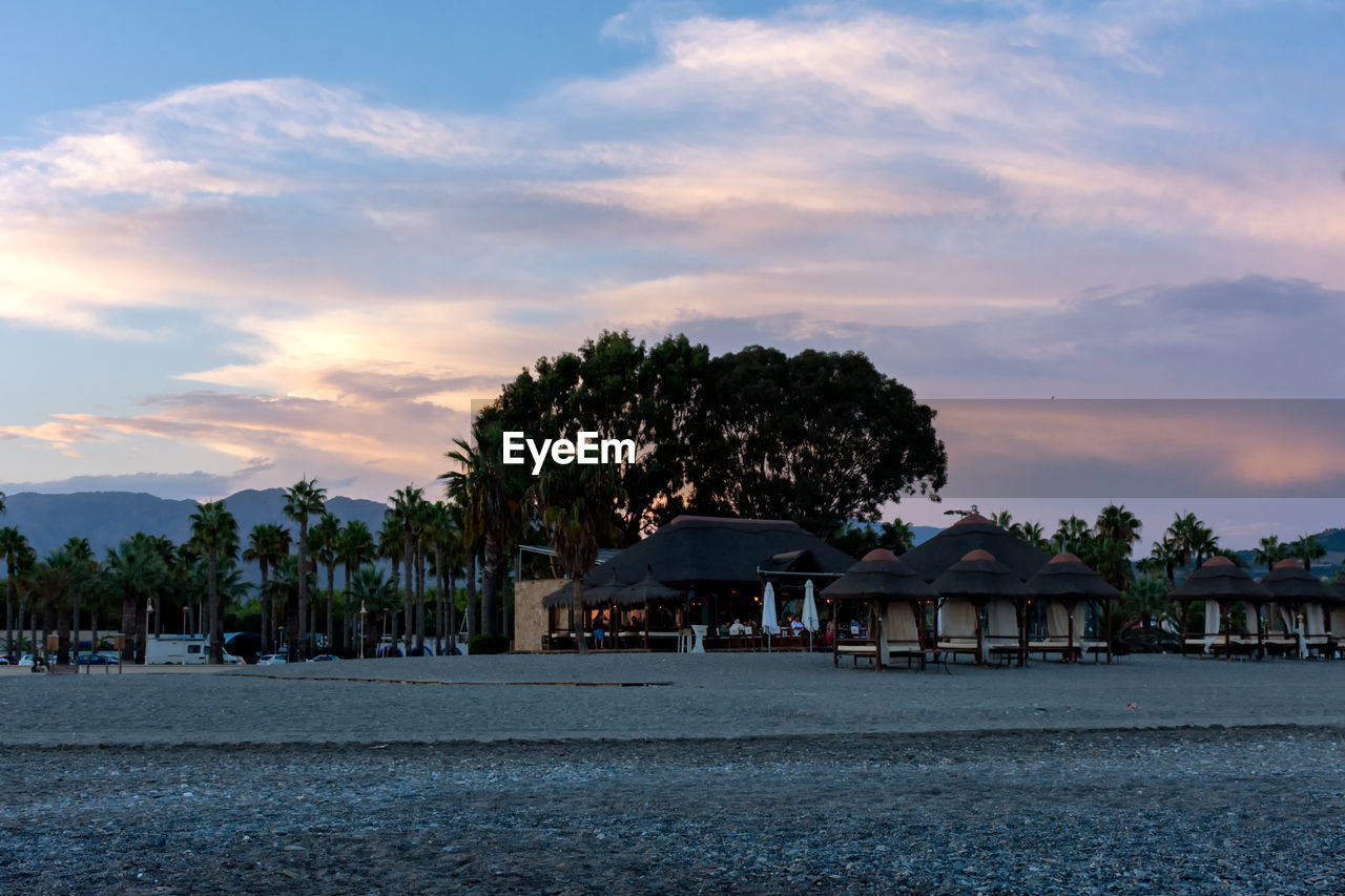 sky, tree, architecture, water, sea, horizon, dusk, tropical climate, cloud, palm tree, shore, beach, sunset, nature, built structure, coast, evening, ocean, travel destinations, plant, land, beauty in nature, building exterior, building, travel, house, tranquility, holiday, scenics - nature, coconut palm tree, environment, tourism, vacation, trip, no people, outdoors, landscape, bay, city, tranquil scene, idyllic, island, stilt house, hut, residential district, body of water, tourist resort, reflection, blue