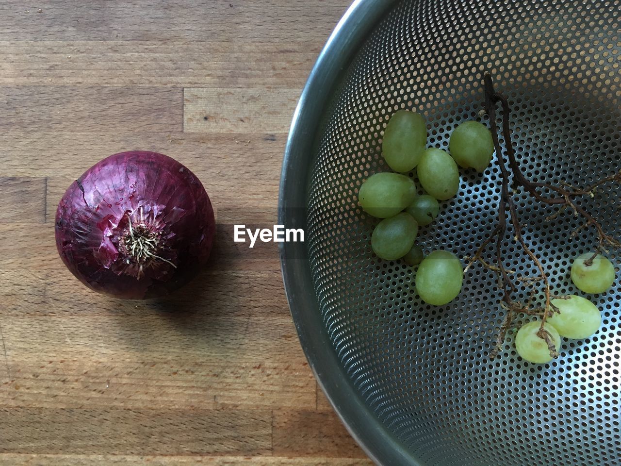 Directly above shot of grapes in strainer by onion on table