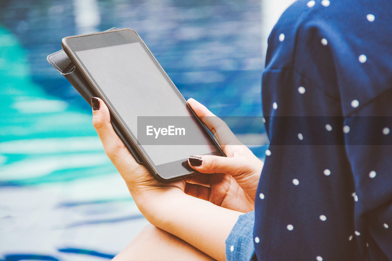 Cropped hands of woman using digital tablet while sitting at poolside