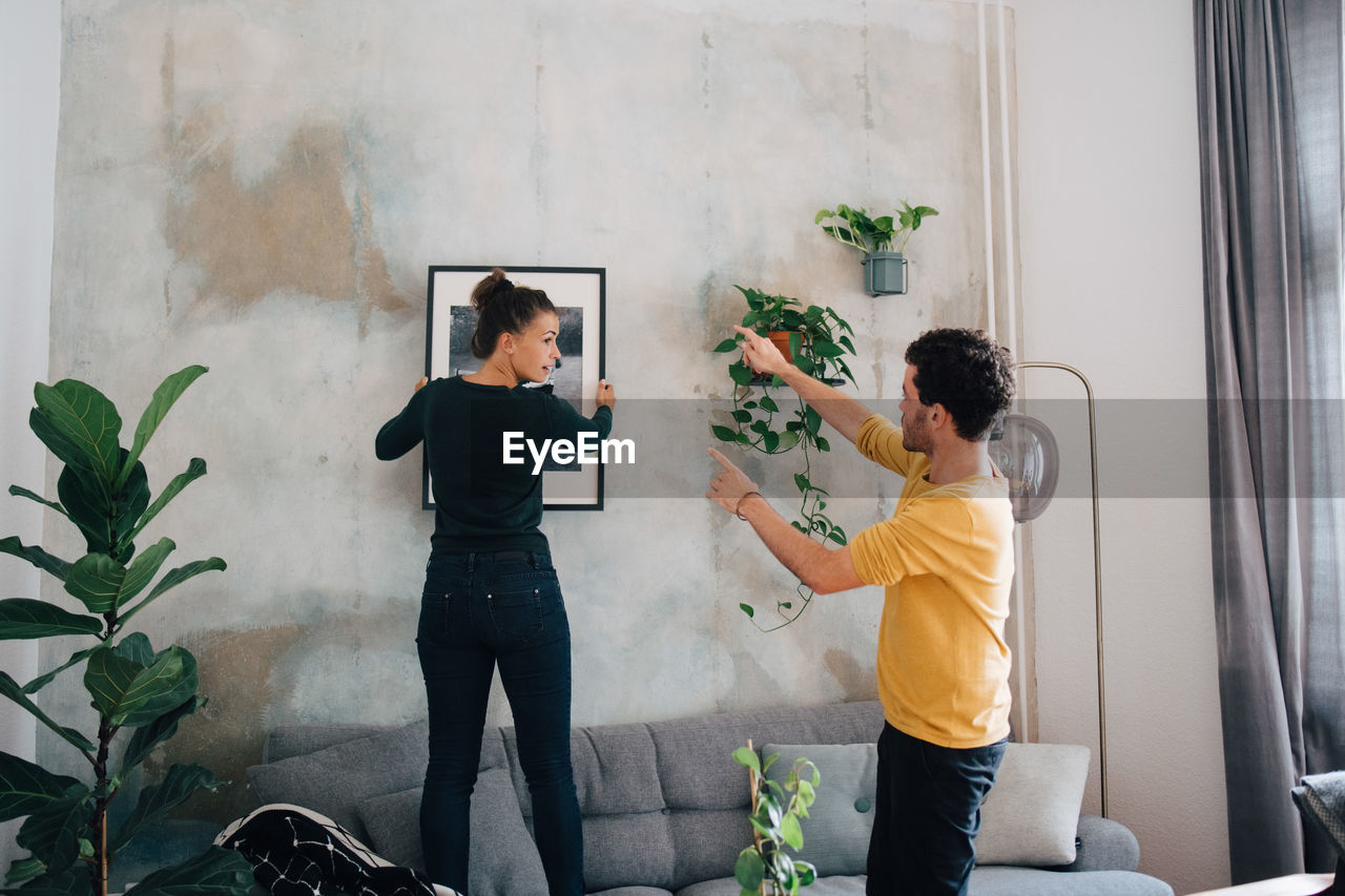 Boyfriend guiding girlfriend in hanging picture frame on wall at new home