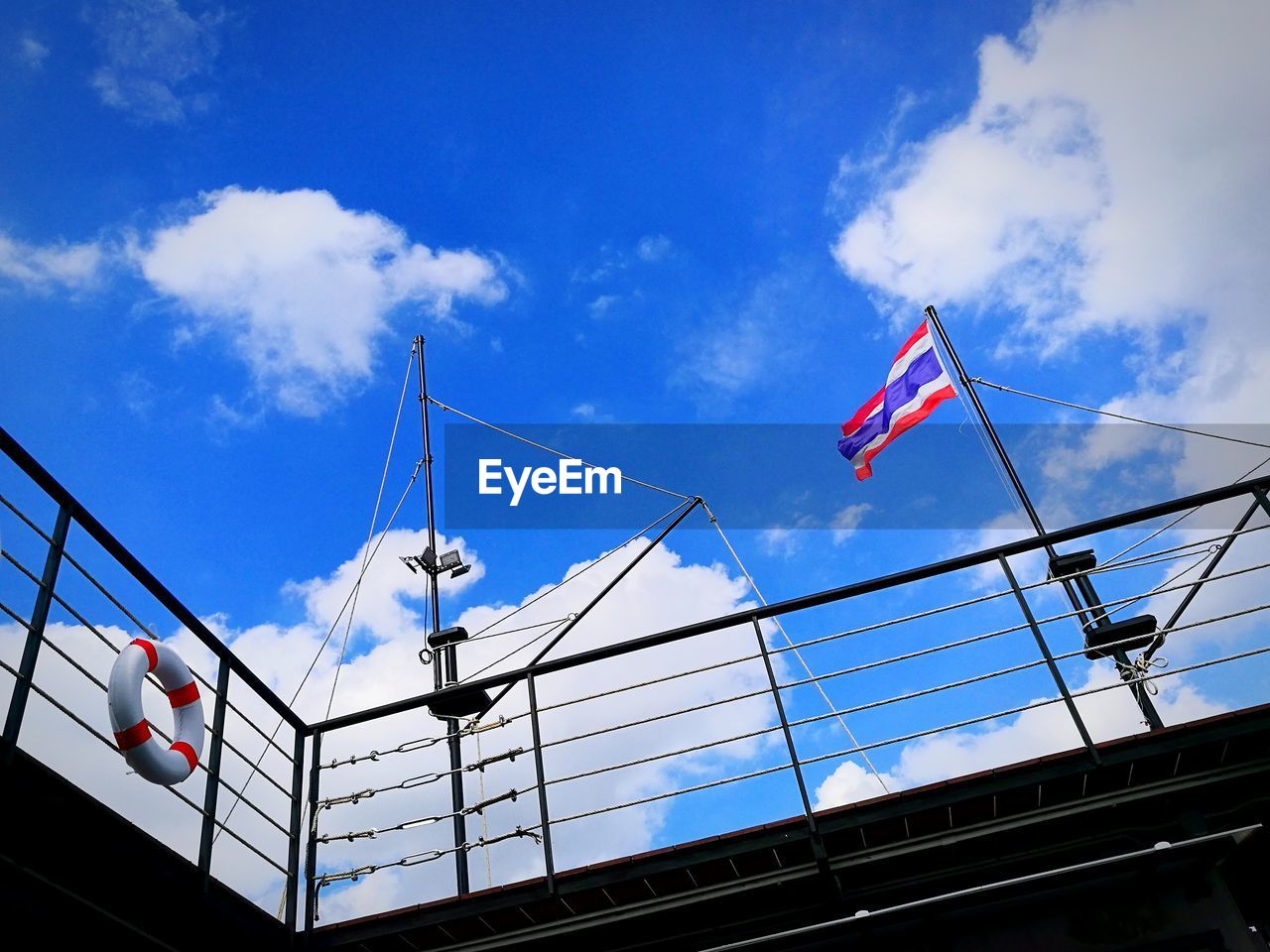 Low angle view of flag and life belt on railing of ship against sky