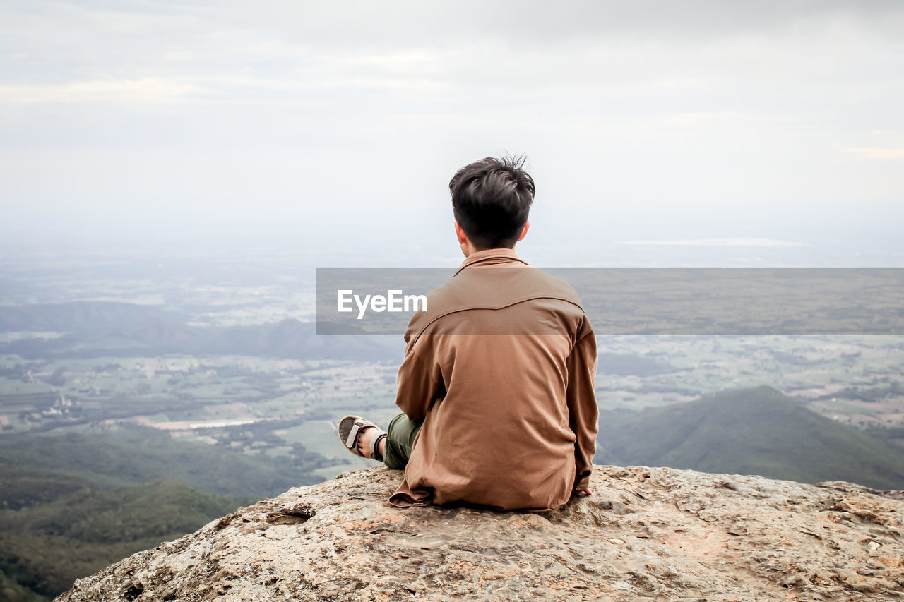 Rear view of woman sitting on mountain against sky