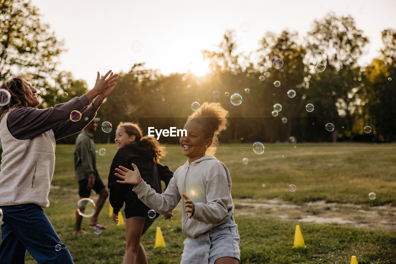 Girl playing amidst bubbles with friends in playground at summer camp