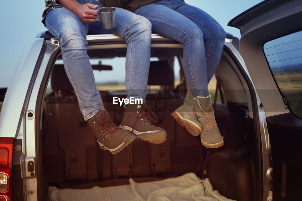 Low section of couple sitting on car roof