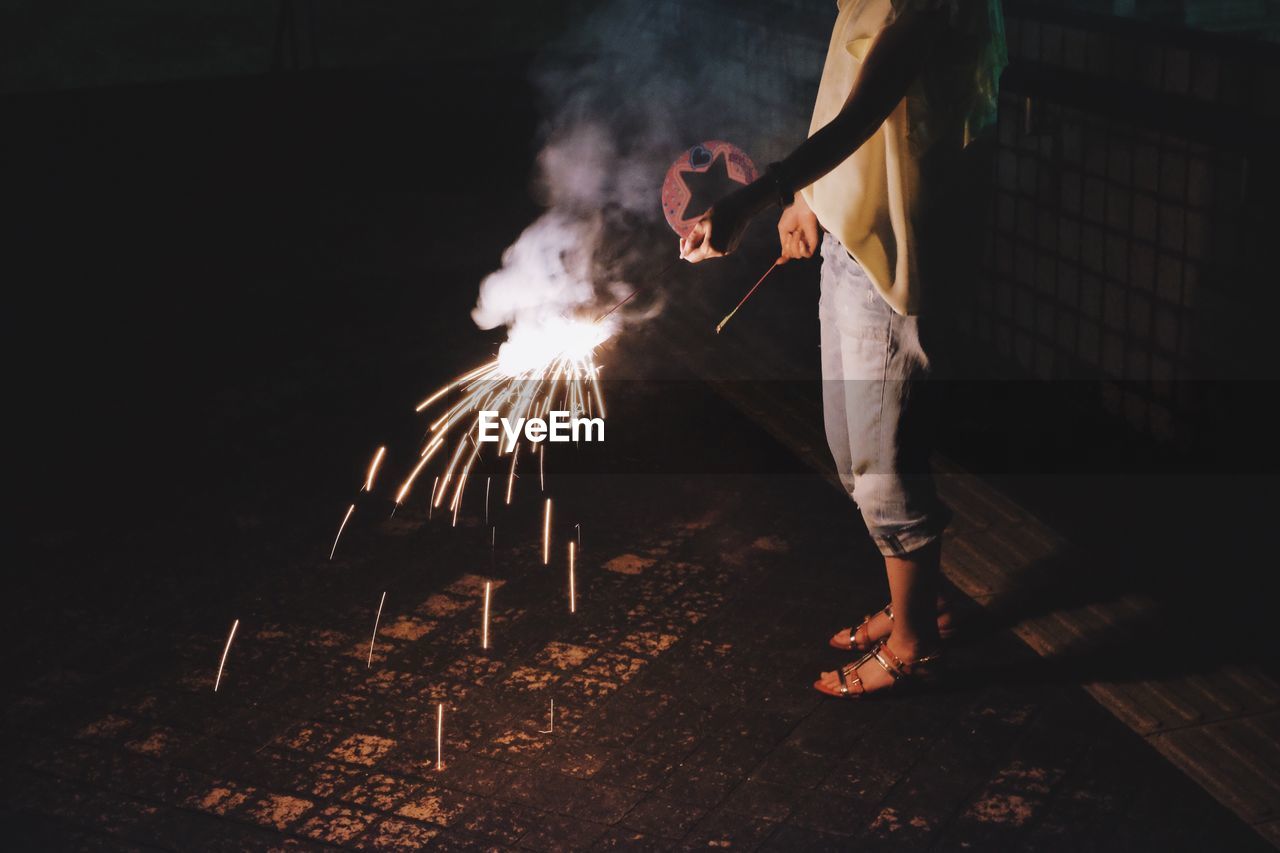 Man with woman holding sparkler on footpath at night