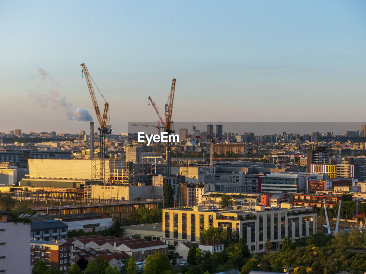High angle view of cranes and buildings against sky during sunset