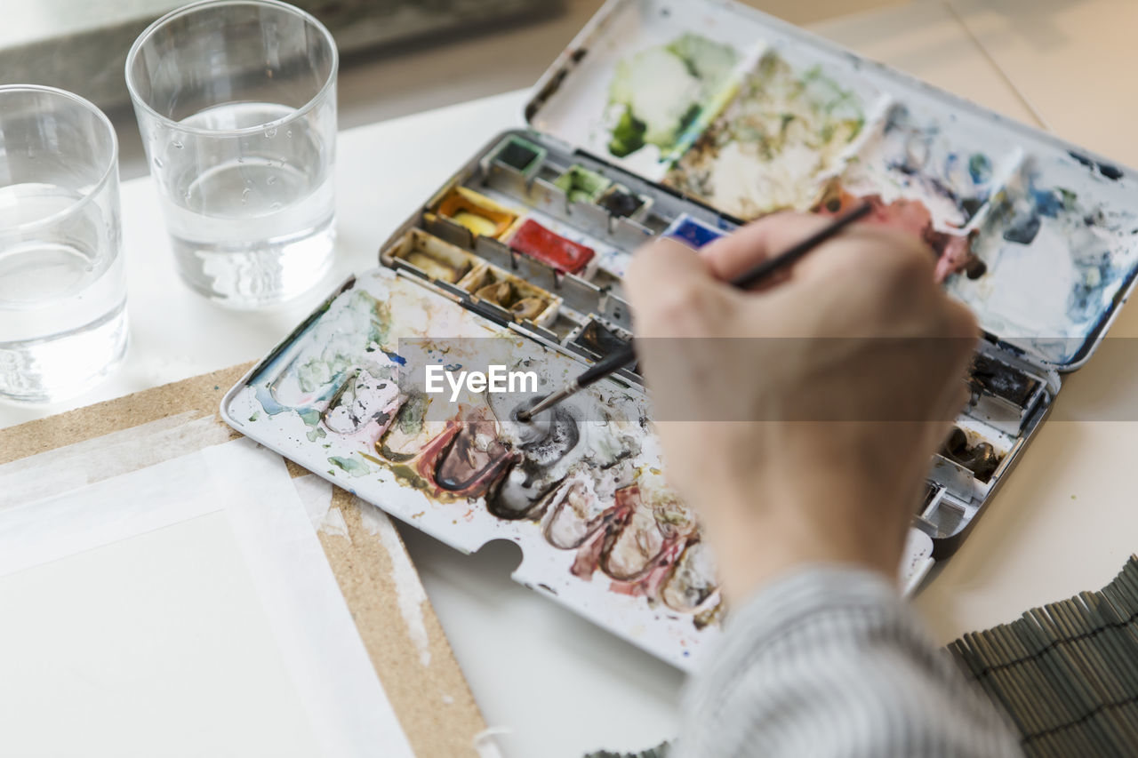 Cropped image of artist mixing watercolor paints while working in creative office