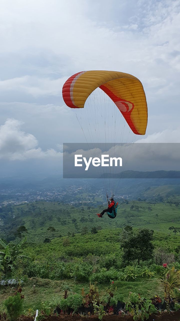 Man paragliding over landscape against sky