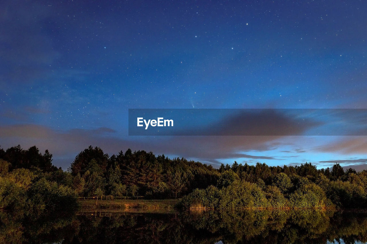 A starry sky in the clouds and a comet over a forest lake just after sunset..