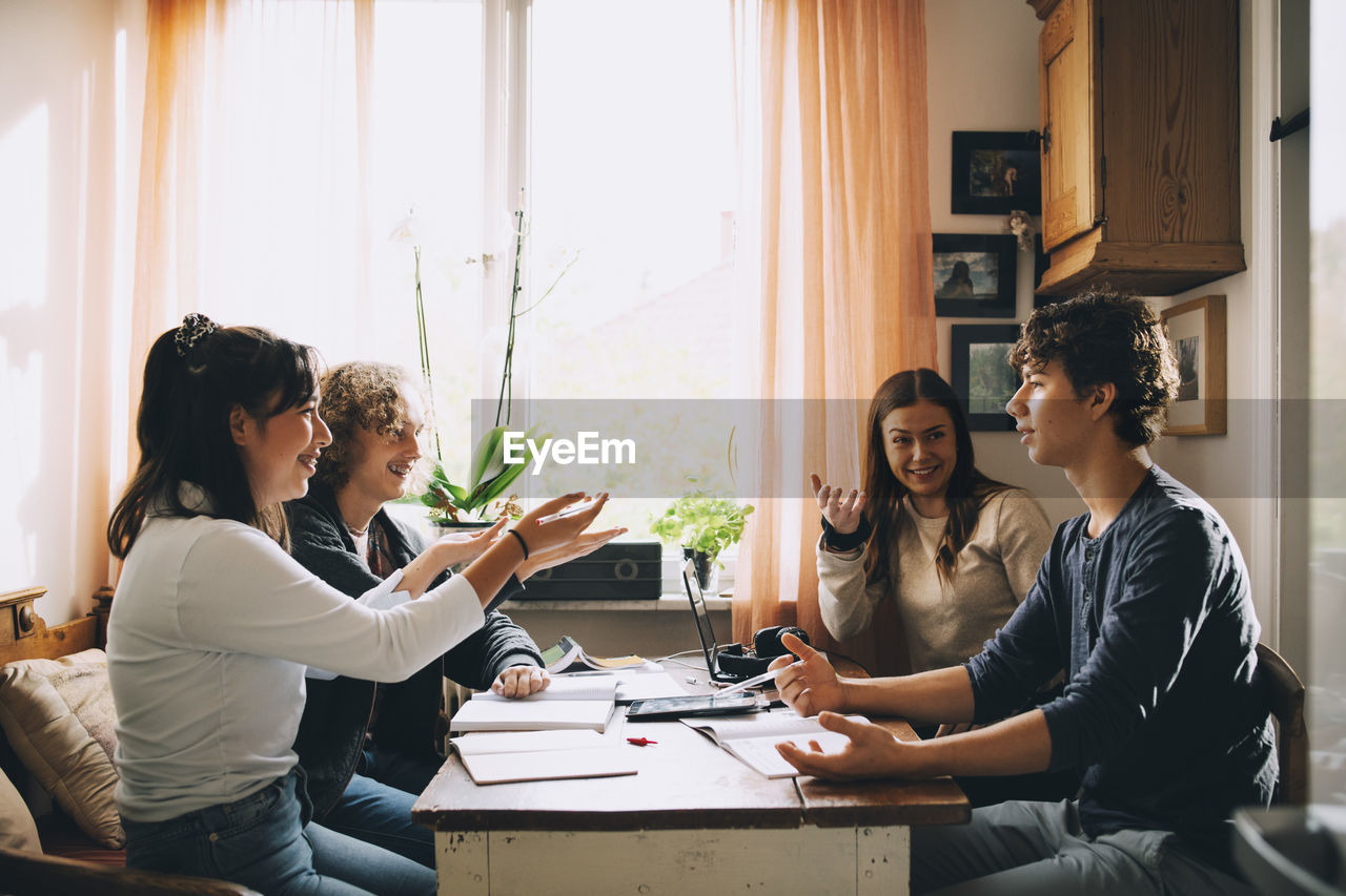 Cheerful friends discussing while studying together at table