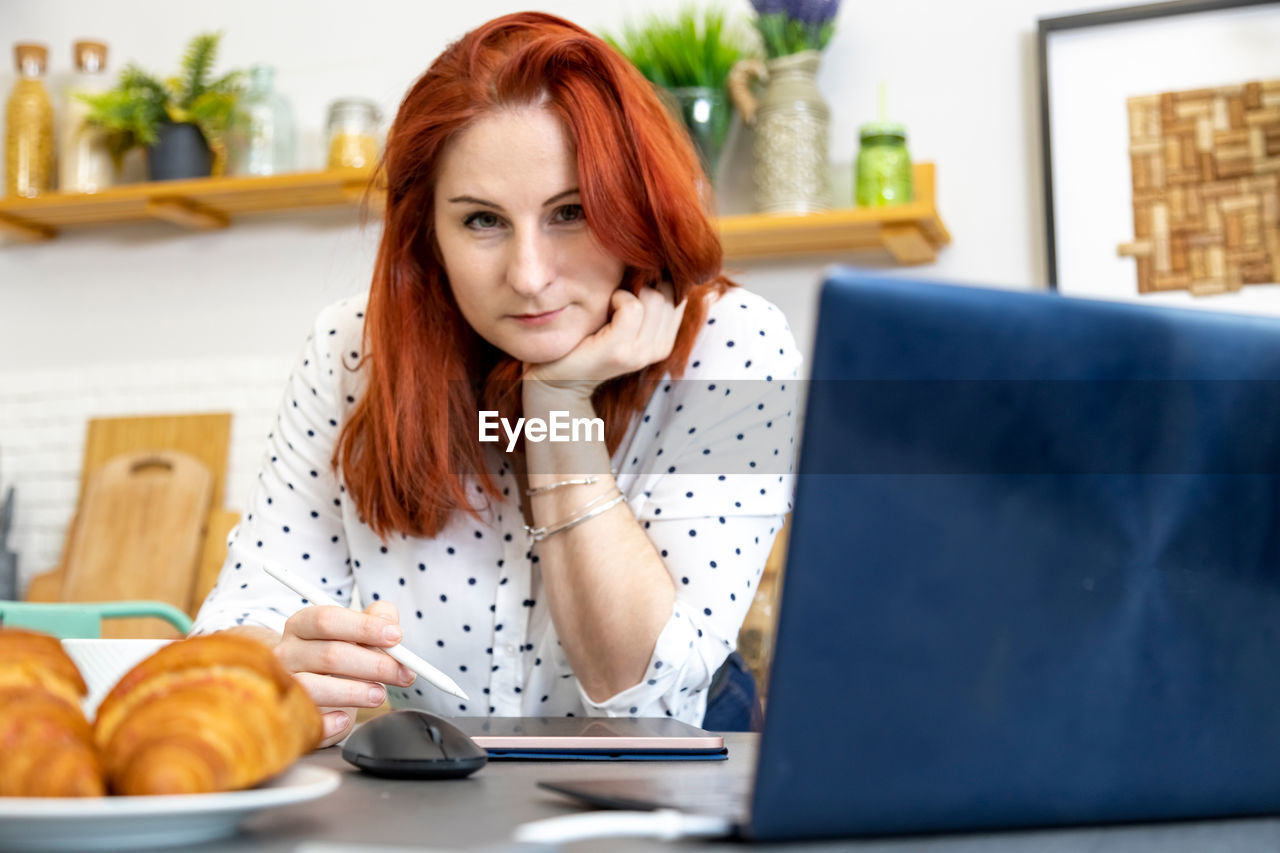 Woman using laptop while sitting at home. young woman sitting in kitchen and working on laptop.