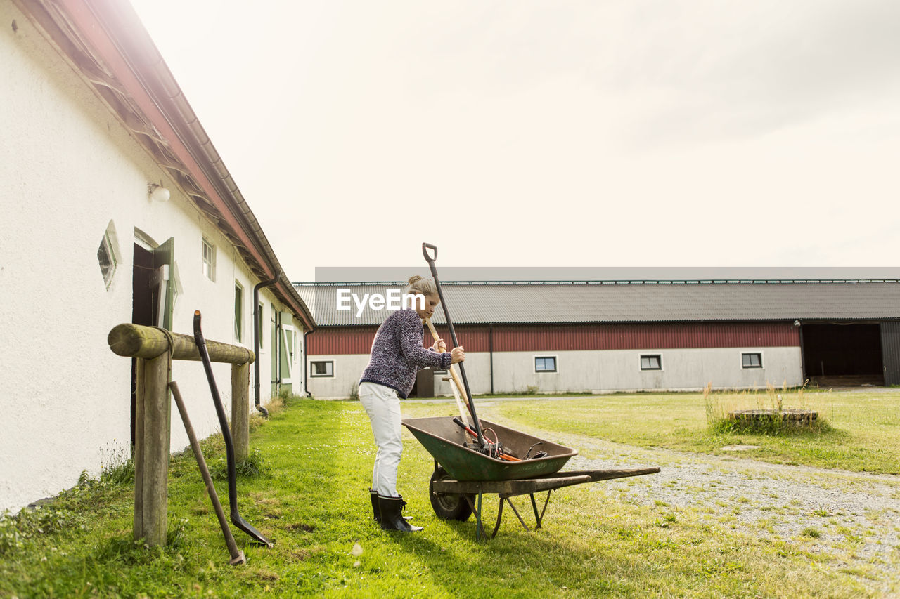 Female farmer removing work tools from wheelbarrow at farm