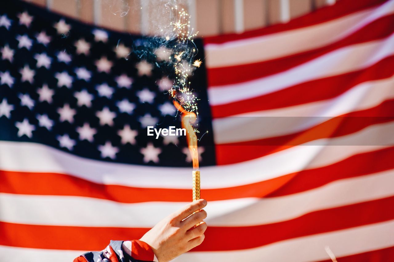 Cropped hand holding lit firework against american flag