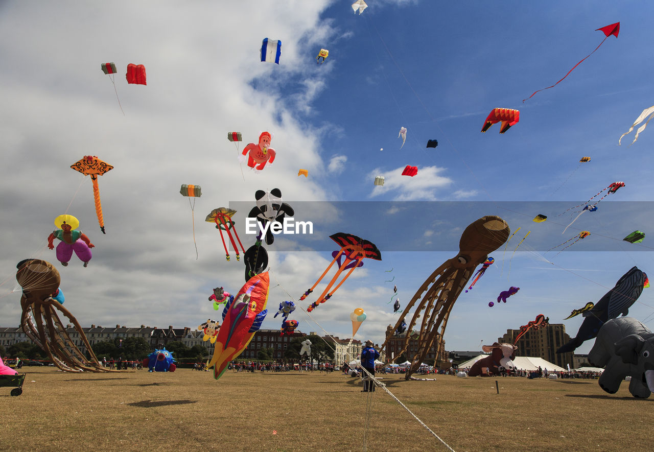 Low angle view of people flying kites against a cloudy sky on a sunny day at southsea kite festival. 