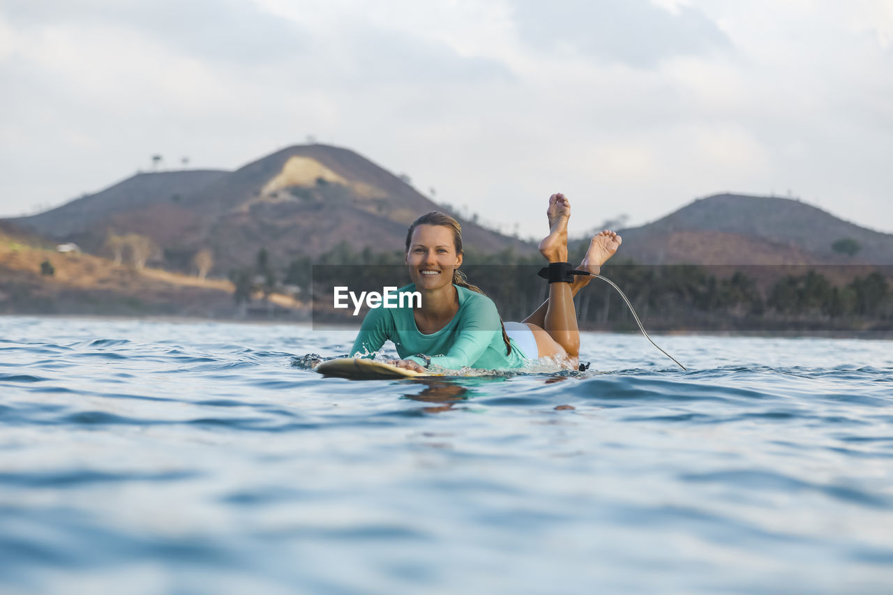 Smiling young woman lying on surfboard