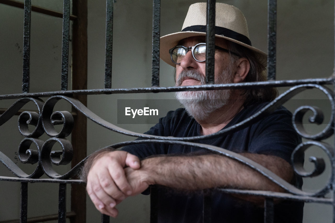 Bearded man, hat and black t-shirt looking through a window