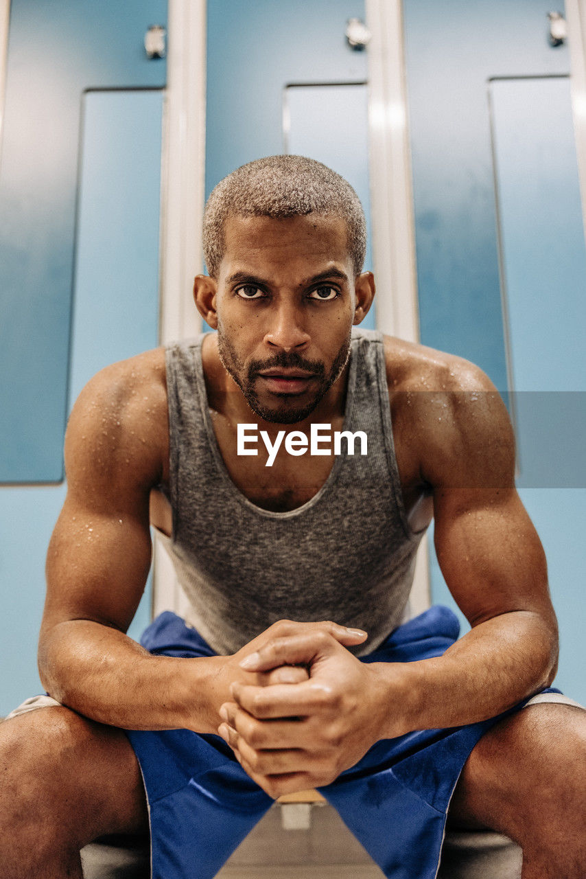 Determined male athlete with muscular build sitting in locker room