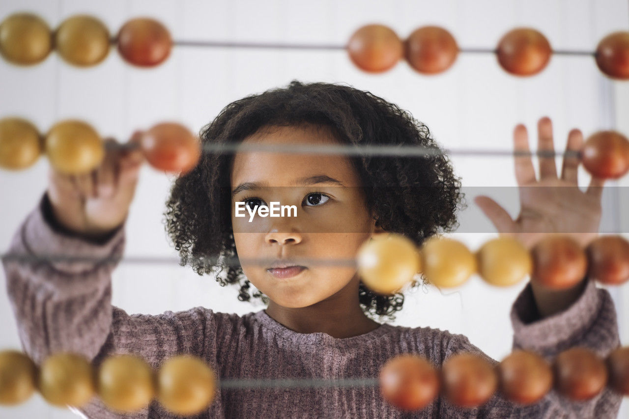 Schoolgirl with curly hair learning to count using abacus in classroom at kindergarten