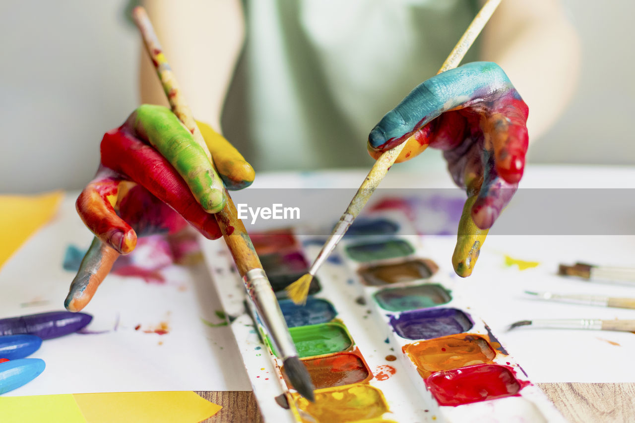 Cropped hand of boy holding paintbrush over palette while painting at classroom