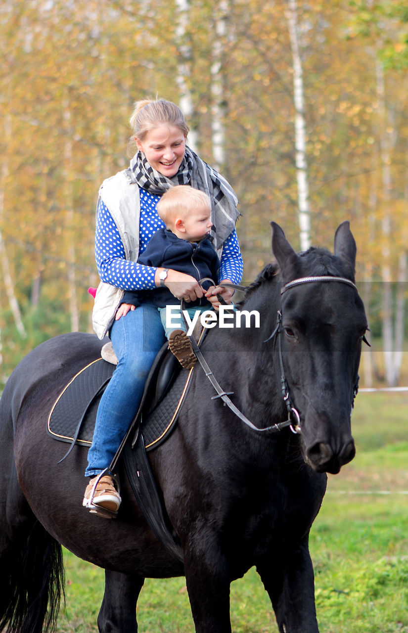 Woman sitting with baby boy on horse at field during autumn