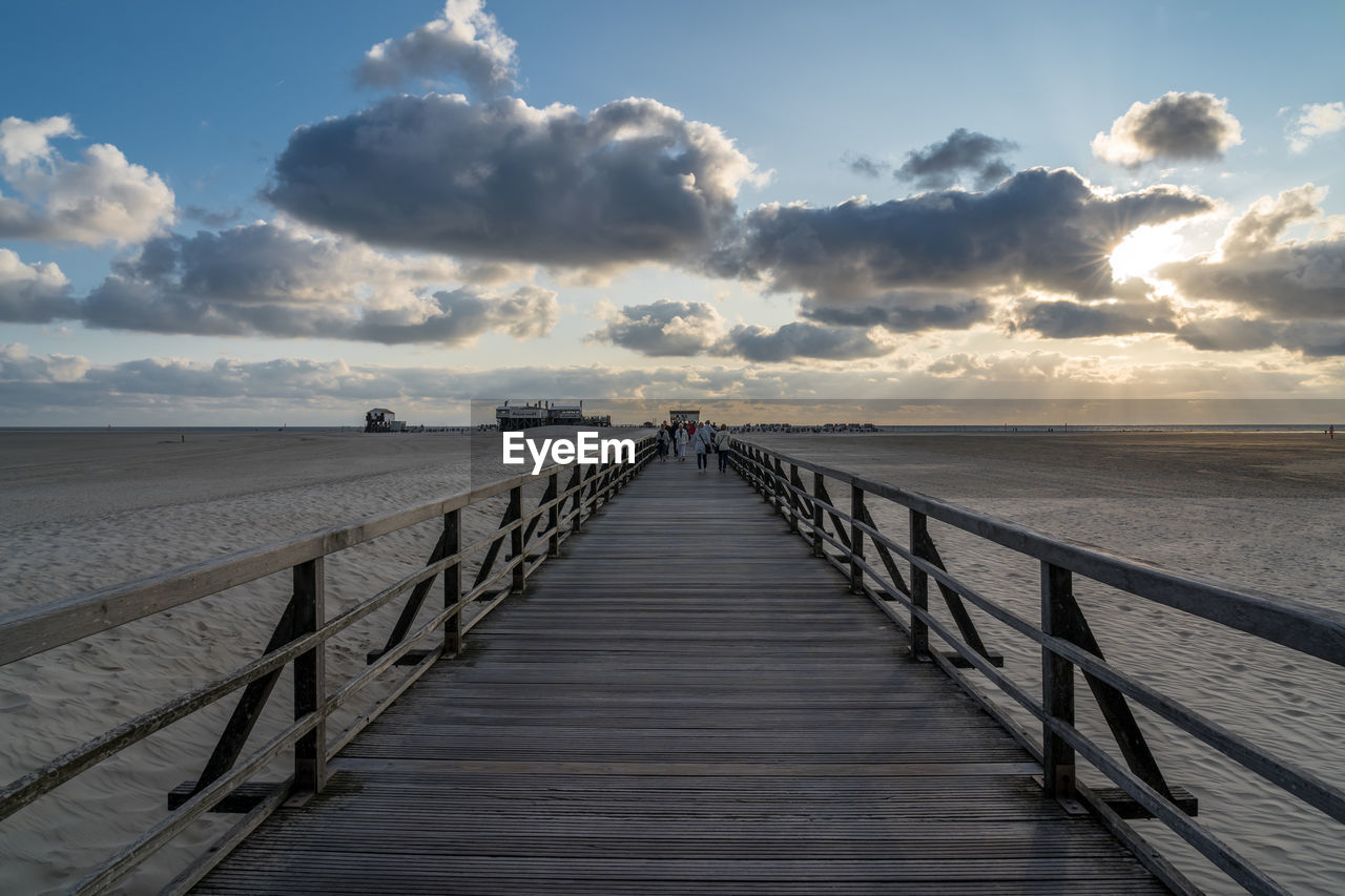 Boardwalk leading towards sea against sky during sunset