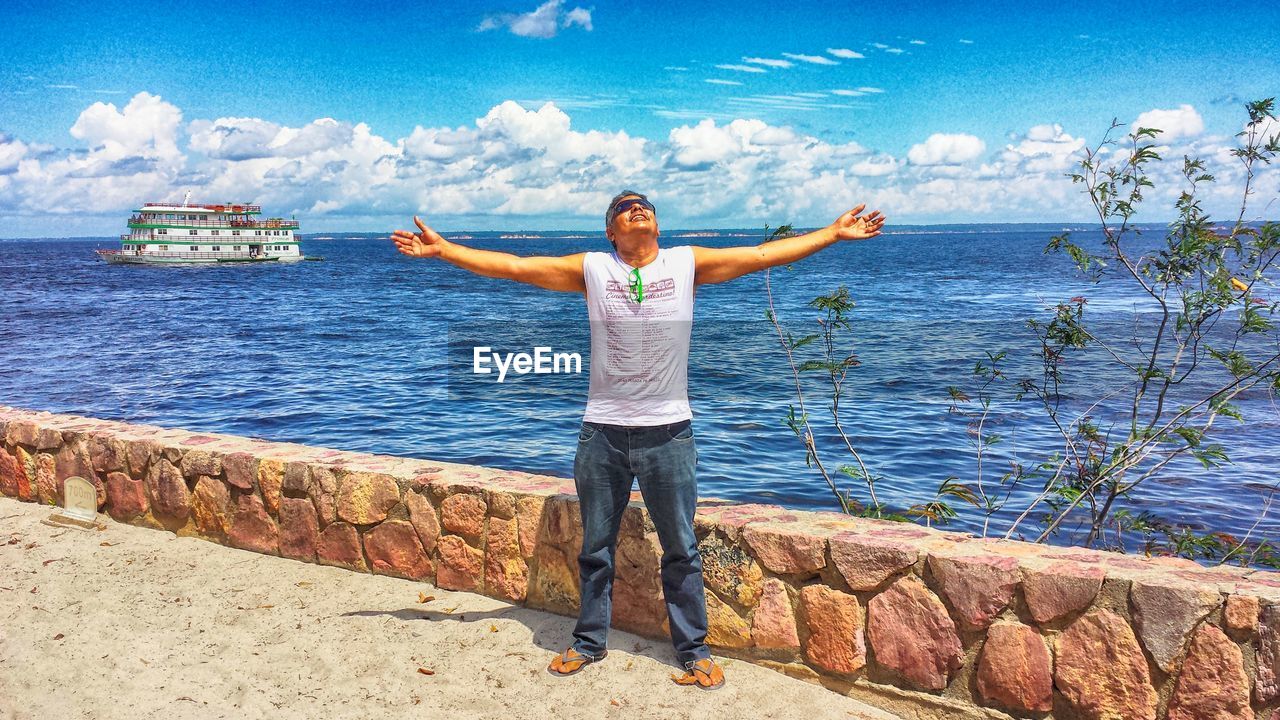 Full length of man with arms outstretched standing against sea