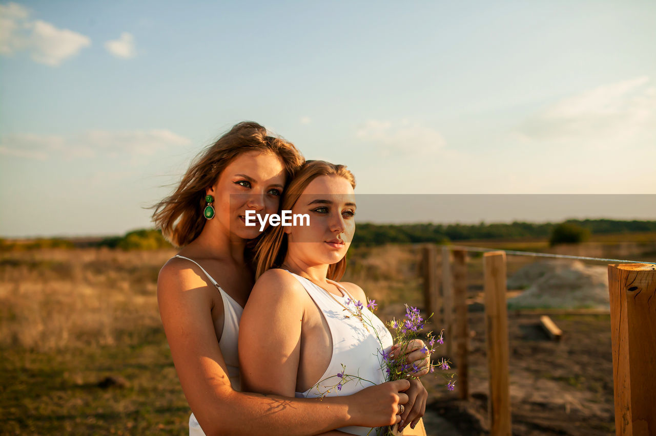 Portrait of two young women on field against sky