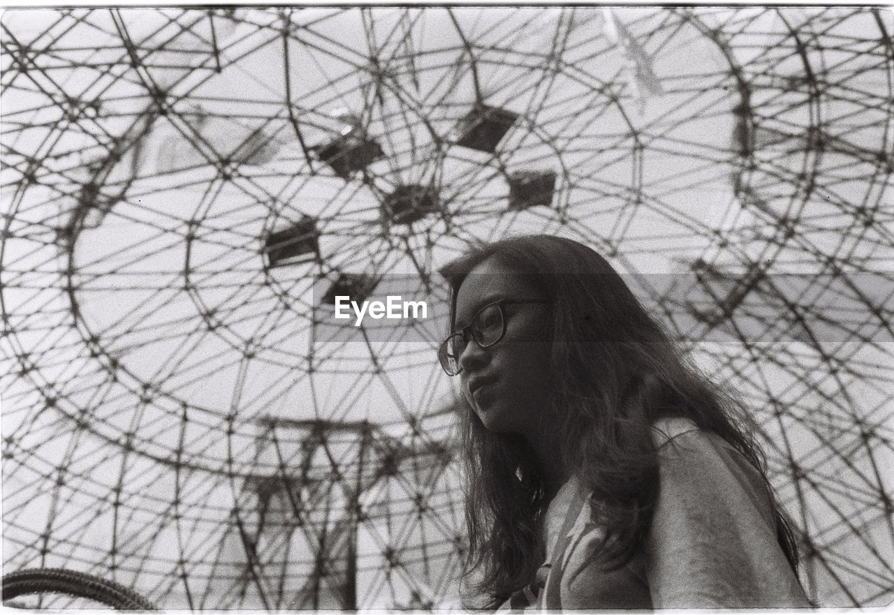 Low angle view of young woman looking away against ferris wheel