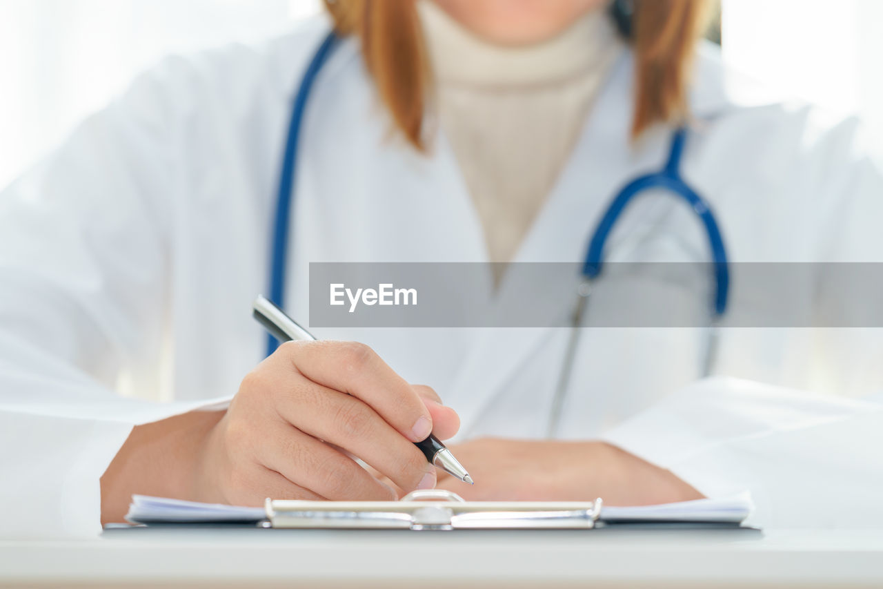 Midsection of female doctor writing prescription on clipboard in hospital