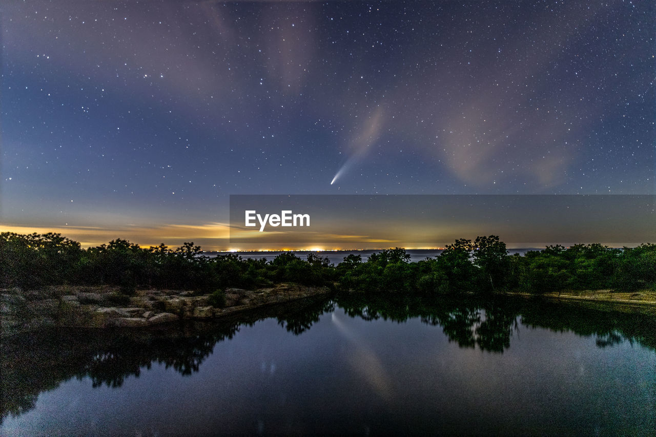 Comet neowise above the ocean horizon reflecting in the water below.