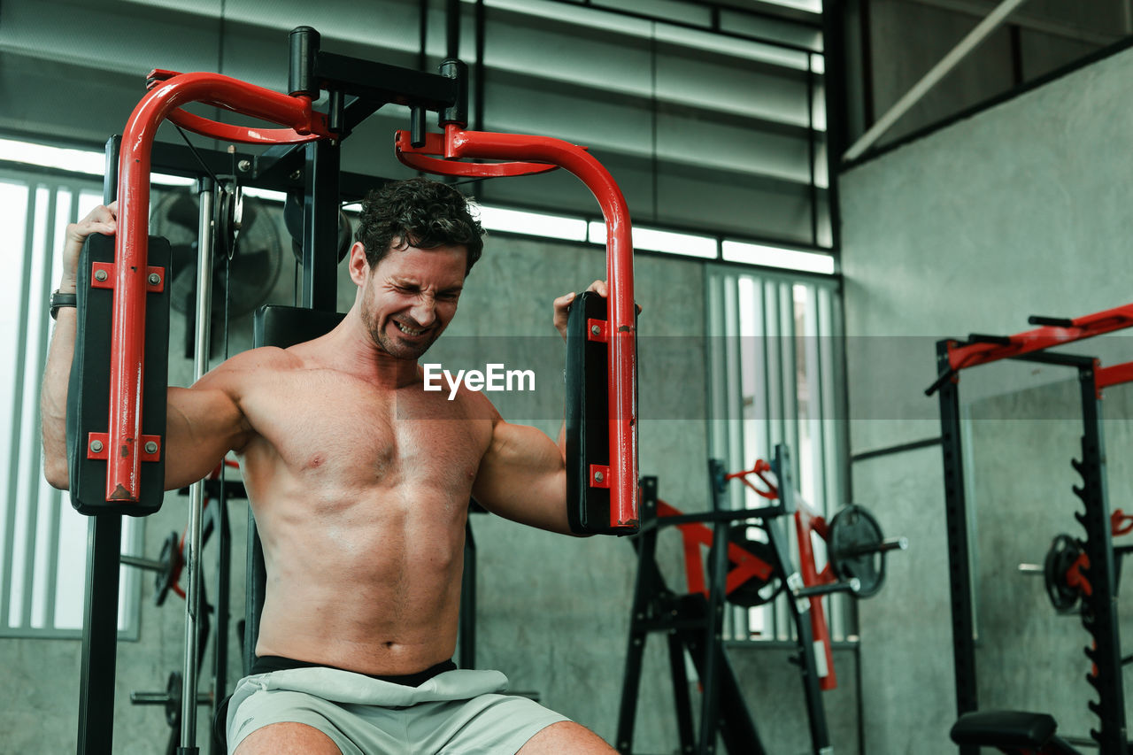 MIDSECTION OF SHIRTLESS MAN SITTING ON MIRROR