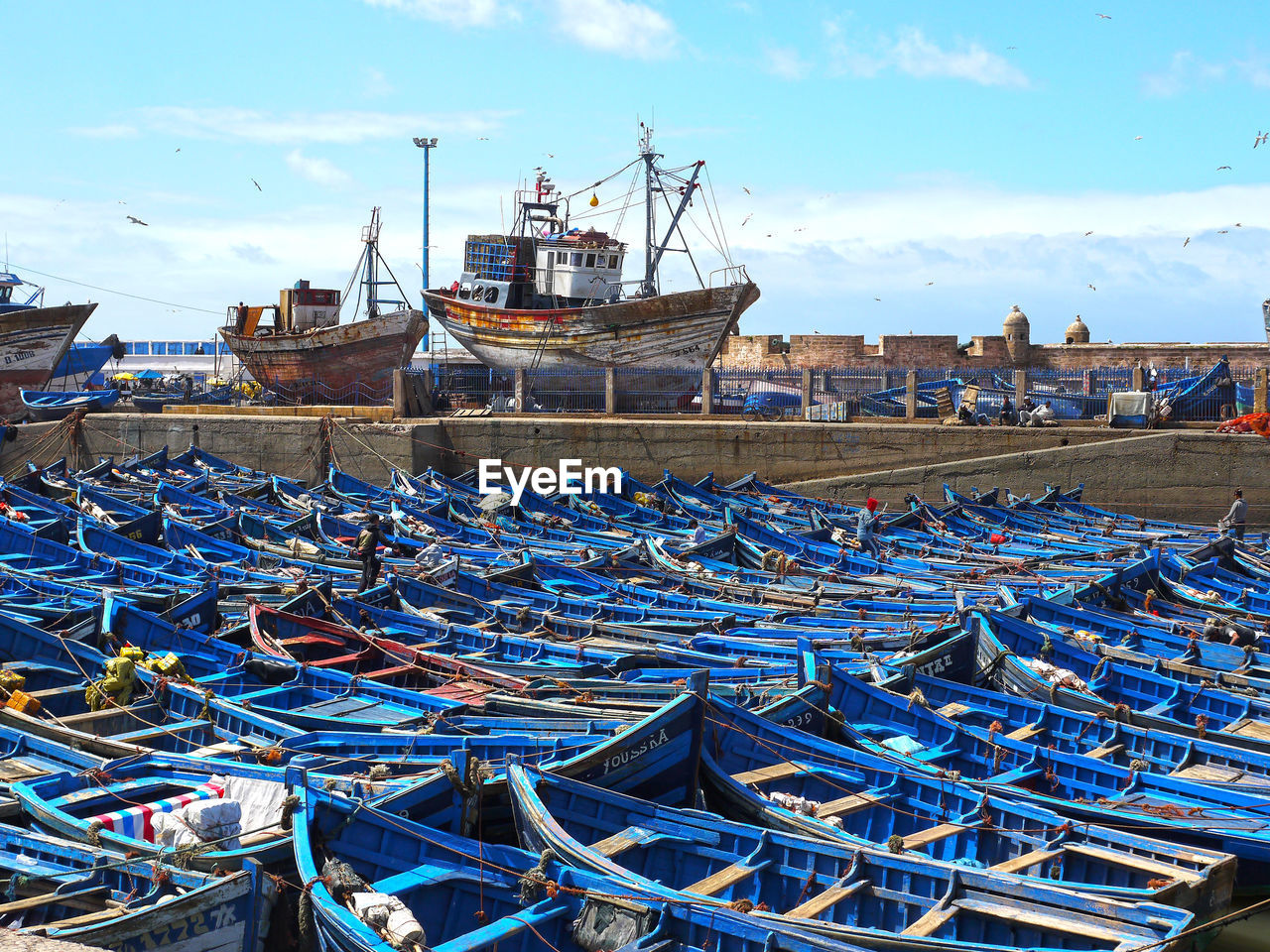 Fishing boats moored at harbor against blue sky