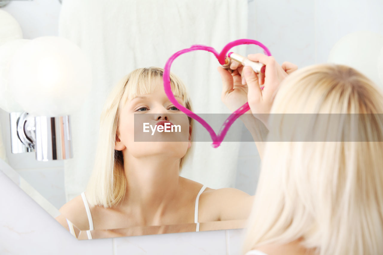 Woman drawing heart shape with lipstick on mirror