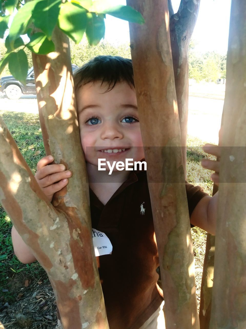 PORTRAIT OF HAPPY BOY STANDING AGAINST TREE