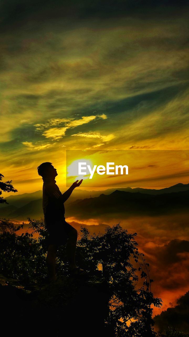 SILHOUETTE MAN STANDING AGAINST SUNSET SKY