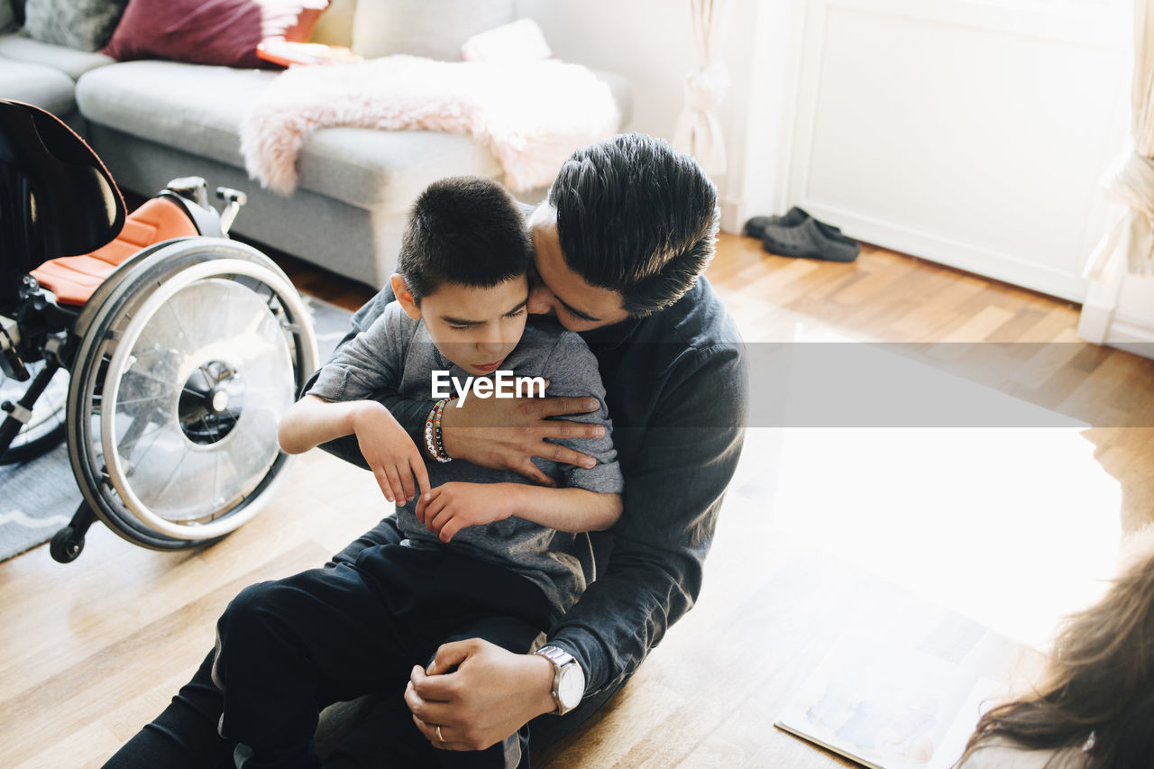 High angle view of father holding autistic son while sitting on floor at home