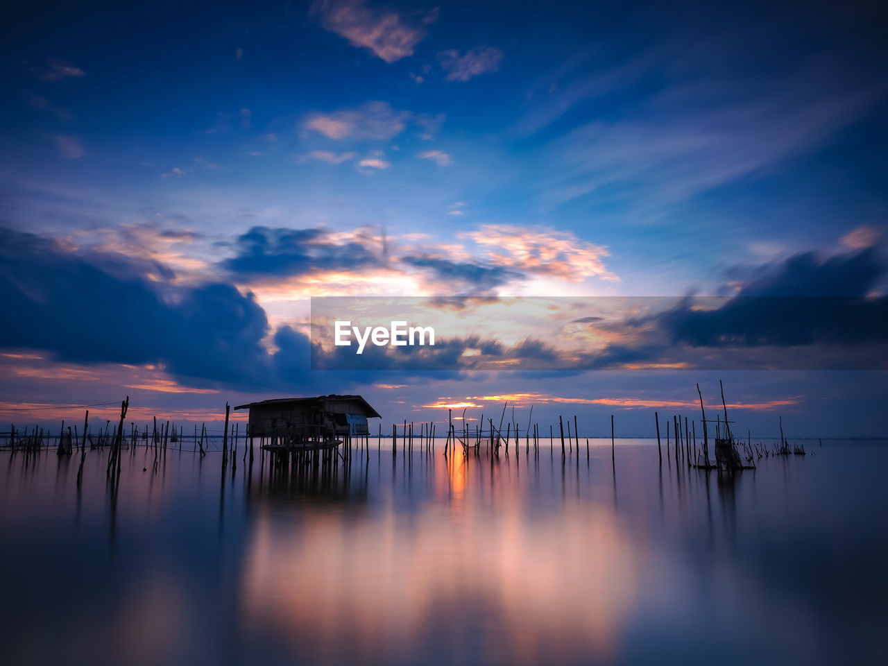 Silhouette wooden posts in sea against sky at sunset