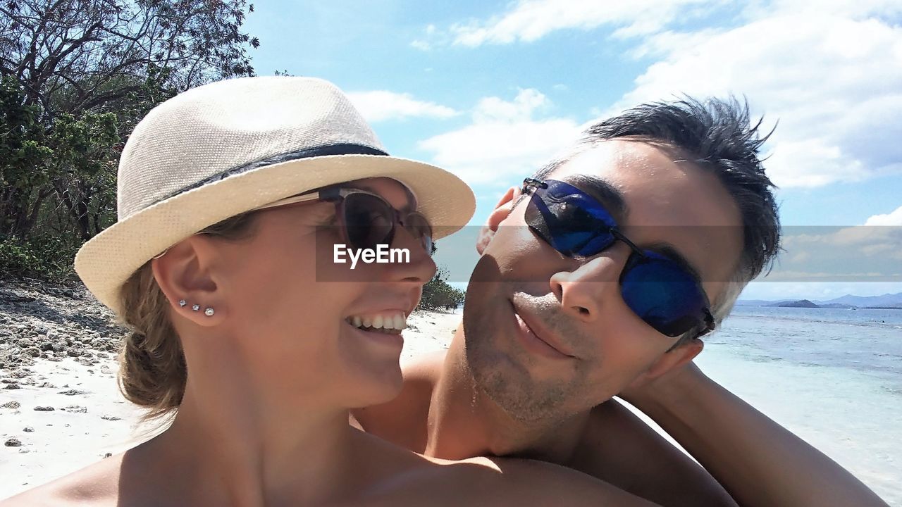 Couple wearing sunglasses at beach against sky