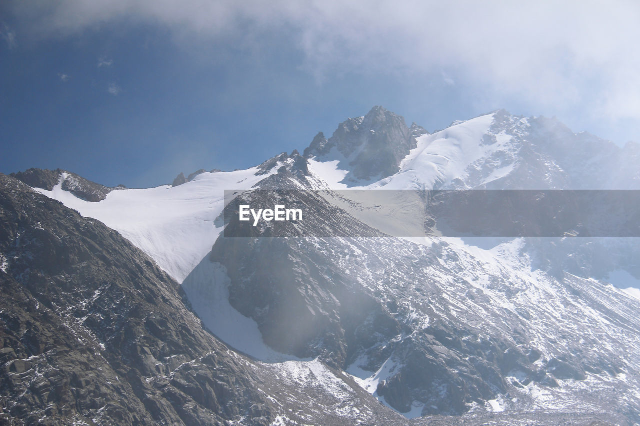 Alpine pointed peaks of mountains covered with snow in clouds, fog and sunlight in winter