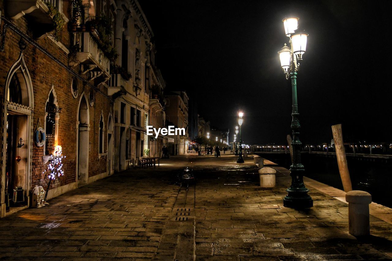 ILLUMINATED STREET LIGHT ON FOOTPATH AGAINST BUILDINGS