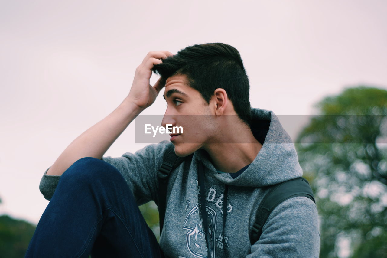 YOUNG MAN LOOKING AWAY AGAINST SKY