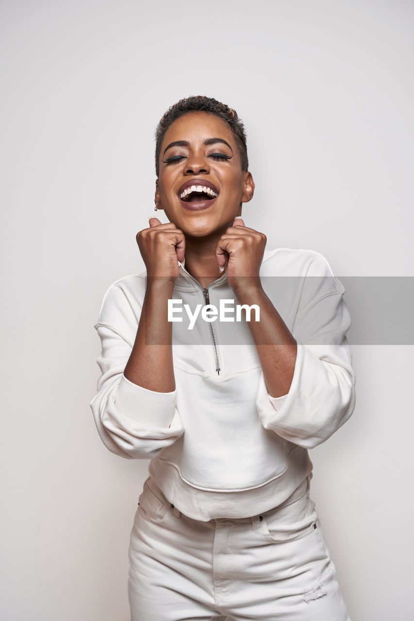 Positive young african american female in stylish apparel with makeup and short hair on light background