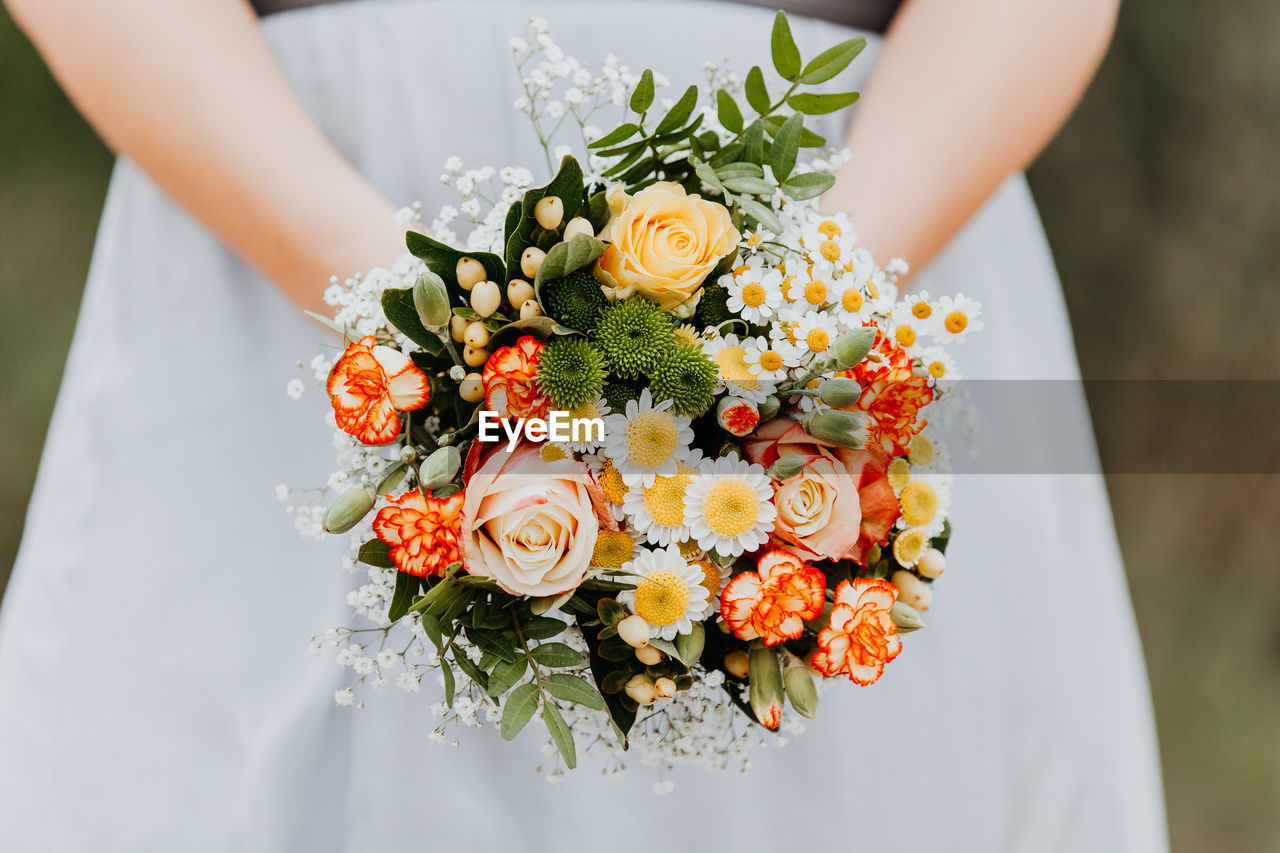 Midsection of bride holding bunch of flowers