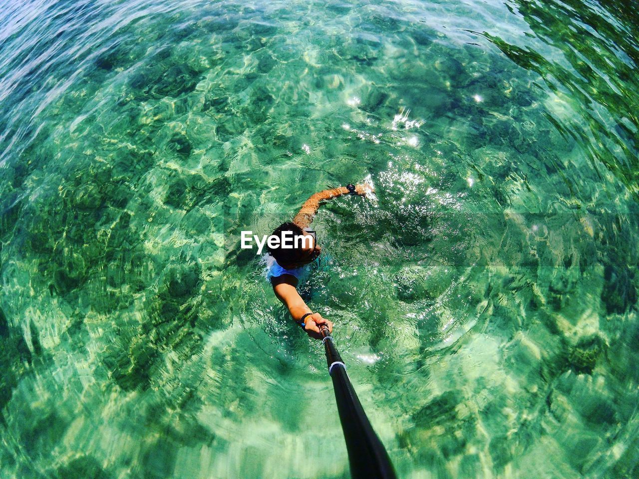 High angle view of man holding monopod while swimming in sea