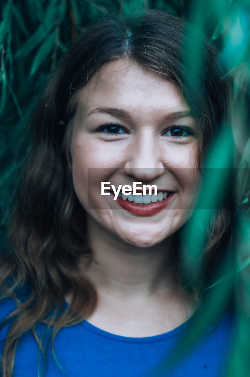 Close-up of smiling girl through plants outdoors