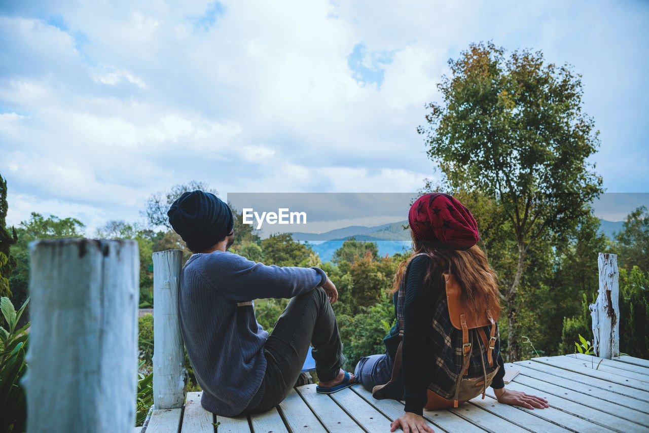 REAR VIEW OF COUPLE SITTING AGAINST PLANTS