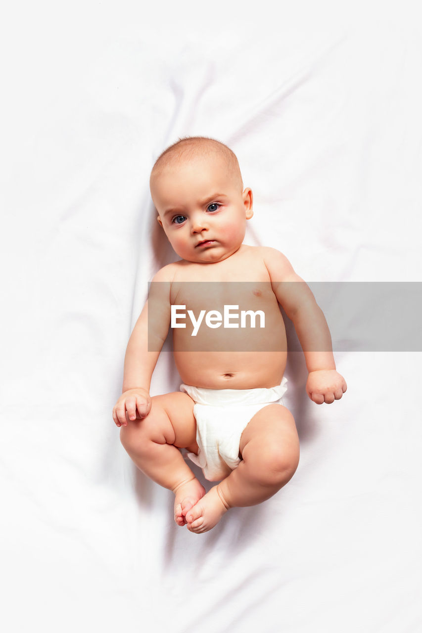 Caucasian funny child in white nappy lies on light background. top view. children's hygiene