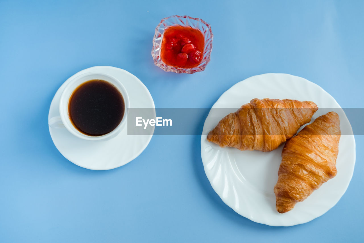 Croissants with jam and morning coffee flat lay. isolated on blue background.